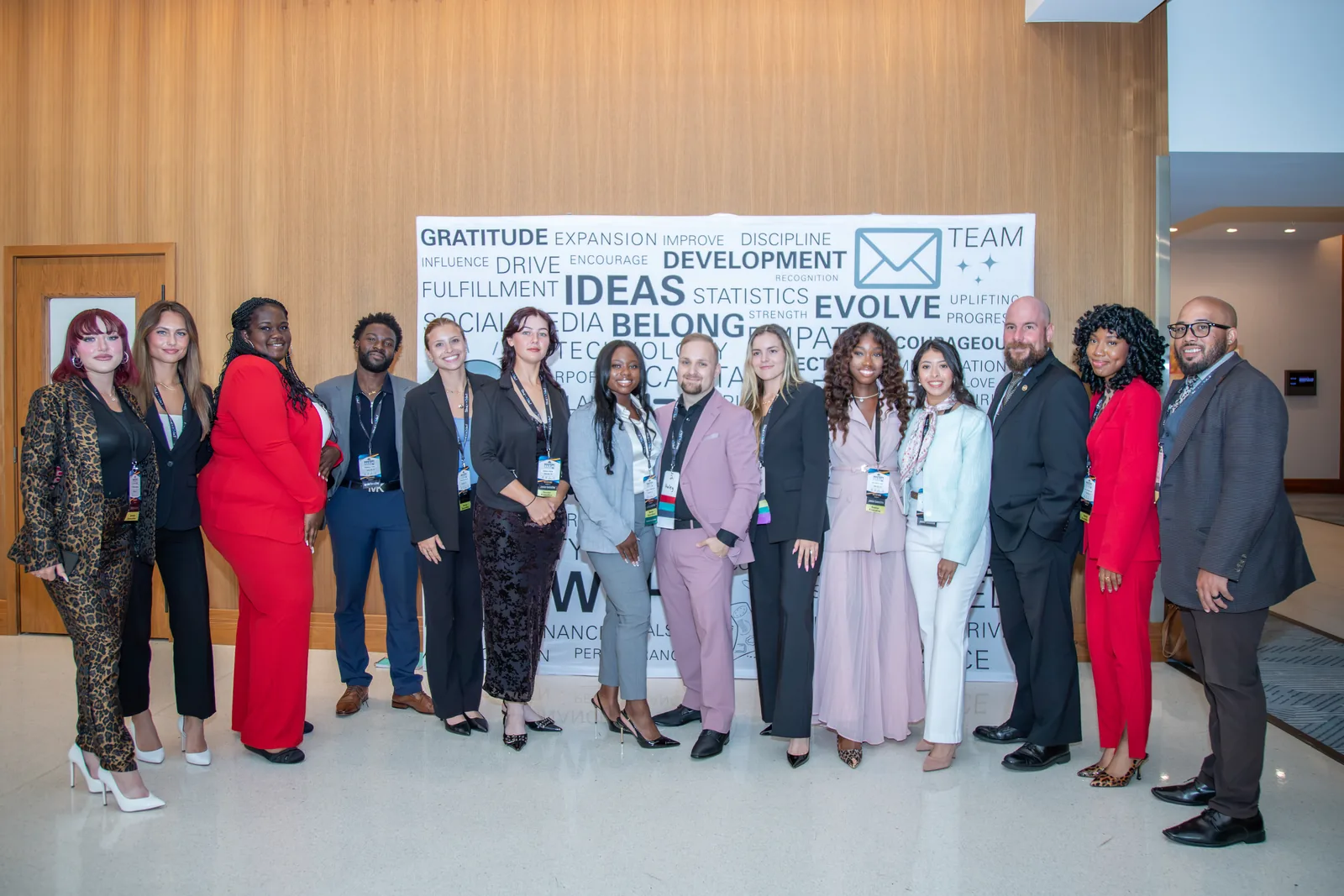 Fifteen Universal Events staff standing in a line in front of a step-and-repeat banner printed with words including GRATITUDE, DEVELOPMENT, IDEAS, EVOLVE, BELONG and TEAM